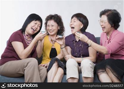 Three senior women and a mature woman holding tea cups and laughing