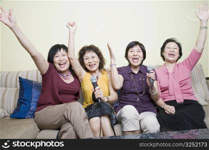 Three senior women and a mature woman singing in front of microphones with their hands raised
