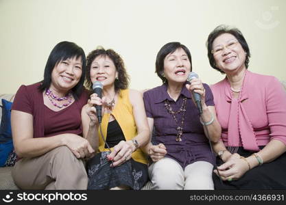 Three senior women and a mature woman singing in front of microphones