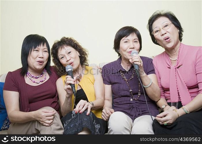 Three senior women and a mature woman singing in front of microphones