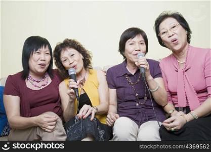Three senior women and a mature woman singing in front of microphones