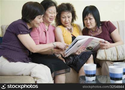 Three senior women and a mature woman sitting on a couch and looking at a photo album