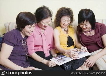 Three senior women and a mature woman sitting on a couch and looking at a photo album