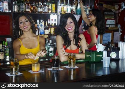 Three sexy young waitresses serve drinks behind bar
