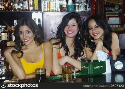 Three sexy young waitresses serve drinks behind bar