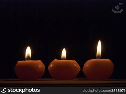 Three short red burning candles on black background