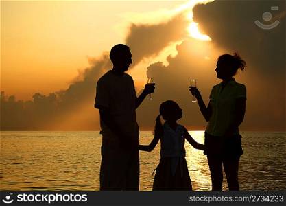 three silhouettes against glossing sea. Daughter between parents. Parents holding glasses