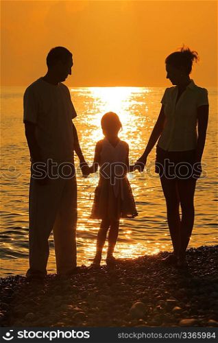 three silhouettes against glossing sea. Parents and daughter.