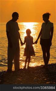 three silhouettes against glossing sea. Parents and daughter.