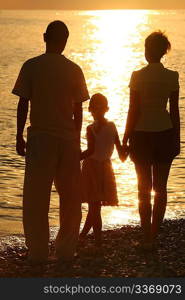 three silhouettes against glossing sea. Parents and daughter.