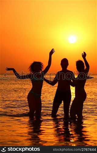 Three silhouettes in sea on sunset