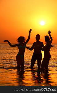 Three silhouettes in sea on sunset