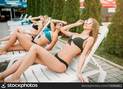 Three slim girls relax on deck chairs outdoors. Sexy women on resort holidays. Three slim girls relax on deck chairs outdoors
