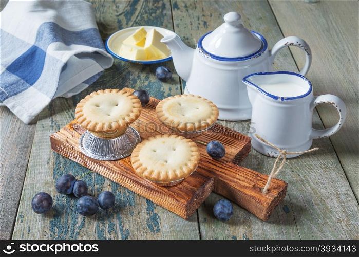 Three small enclosed cake with plums, butter and a creamer and sugar bowl in vintage style
