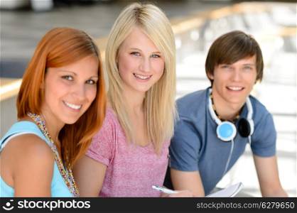 Three smiling college student friends sitting together looking at camera