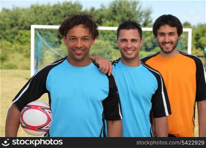 Three smiling footballers in front of goal