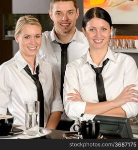 Three smiling server posing in uniform in cafe