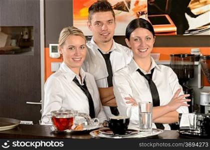Three smiling server posing in uniform in cafe
