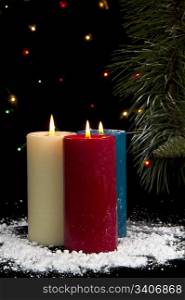 Three snow covered colorful candles burning with fir branch and cones in background