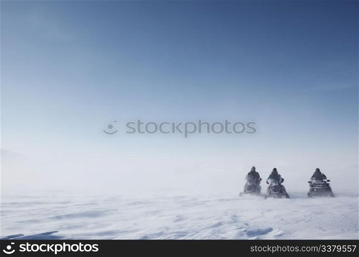 Three snowmobiles on a blowing barren winter landscape