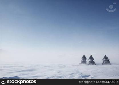 Three snowmobiles on a blowing barren winter landscape