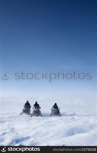 Three snowmobiles on a winter landscape with blowing snow