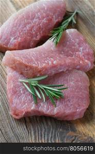 Three steaks of fresh organic meat and two sprigs of rosemary on an old wooden background closeup