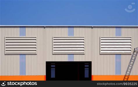Three Steel Louvers on multi colored Aluminium Corrugated Wall with entrance door of Industrial Warehouse Building against blue clear sky background