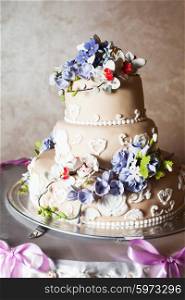 Three-storied wedding cake with violet flowers on a glass stand. Three-storied wedding cake