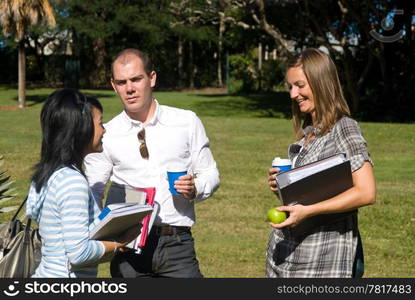 Three students conversing on campus, drinking coffee and holding their notebooks.