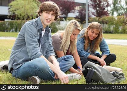 Three students sitting on the grass of a campus.