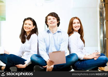 Three students smiling. Image of three students in casual wear sitting on floor and smiling