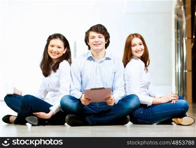 Three students smiling. Image of three students in casual wear sitting on floor and smiling