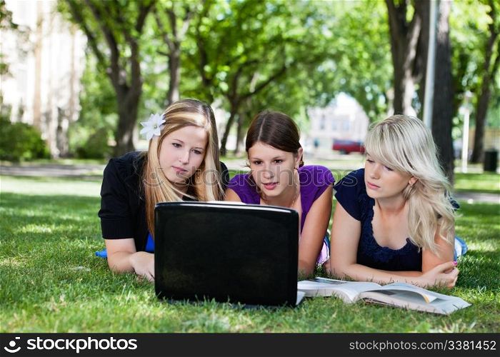Three students working on laptop on campus ground