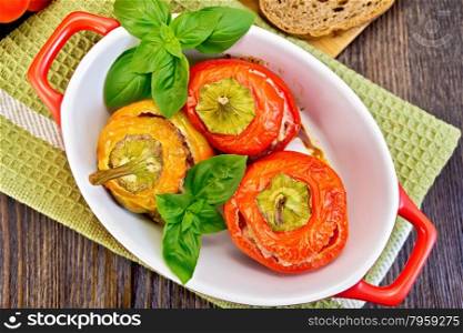 Three sweet peppers stuffed with meat and rice with basil leaves in red brazier on the green napkin, bread on the background of wooden boards on top