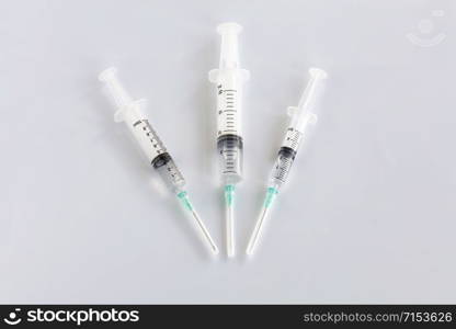 Three syringes of different capacity on the table in the hospital, prepared for injection, copyspace for the text below.. Several different syringes on a white smooth table are filled with mortar and ready for use and point to the lower center.