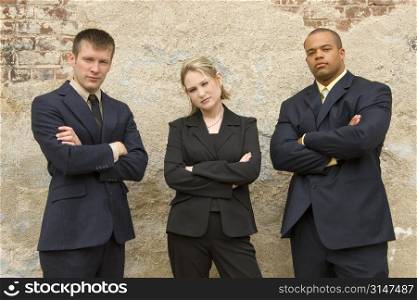 Three team meembers standing outdoors against a grunge brick and plaster wall.