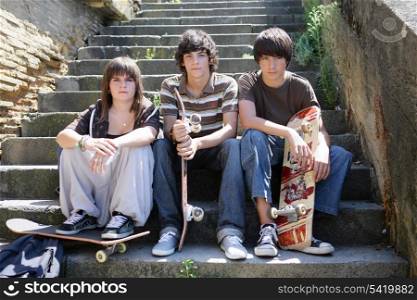 Three teen skateboarders sat on steps