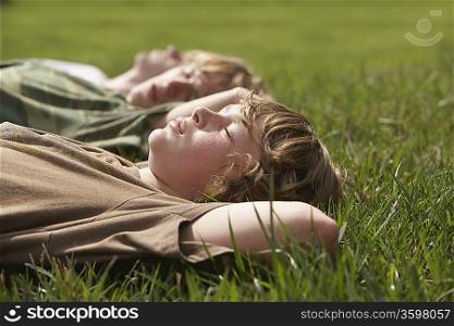 Three teenage brothers (13-17) lying down on grass close up