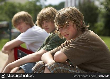 Three teenage brothers (13-17) sitting on street curb portrait