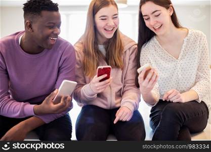 Three Teenage Friends Laughing As They Share Content On Mobile Phones