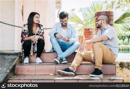 Three teenage friends talking sitting on the stairs, Three young people sitting on the street talking. Concept of friends talking, Three young friends talking sitting on the stairs