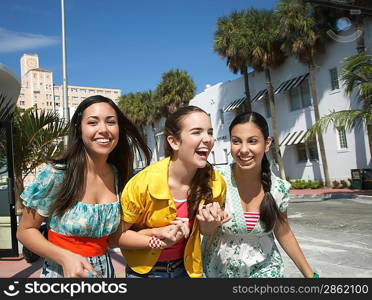 Three teenage girls (16-17) walking on street and laughing