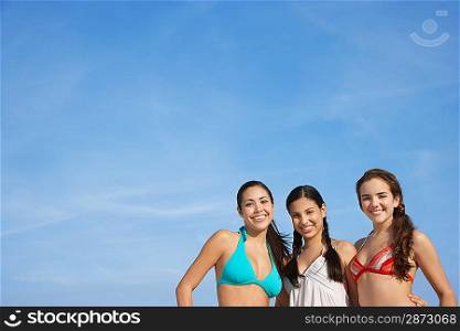 Three teenage girls (16-17) wearing bikinis pictured against sky portrait