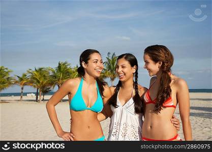 Three teenage girls (16-17) wearing bikinis standing on beach portrait