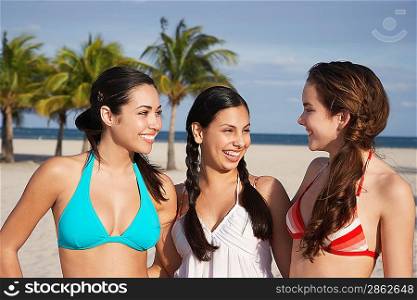 Three teenage girls (16-17) wearing bikinis standing on beach portrait