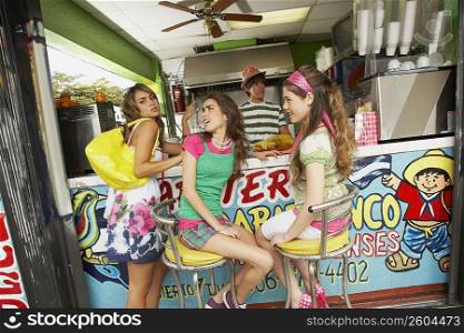 Three teenage girls at a bar counter with a bartender behind them in a juice bar