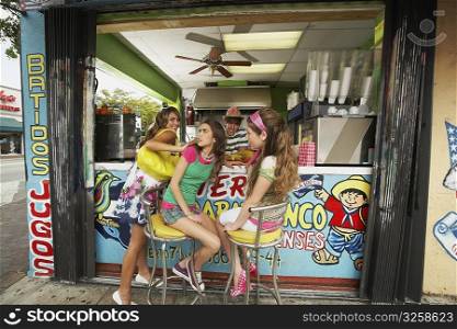 Three teenage girls at a bar counter with a bartender behind them in a juice bar