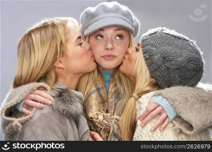 Three Teenage Girls Wearing Cap And Knitwear In Studio Giving Each Other Kiss