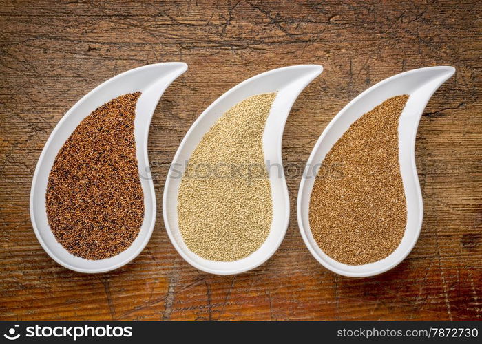 three tiny gluten free grains - kaniwa, amaranth and teff on teardrop shaped bowls against rustic wood